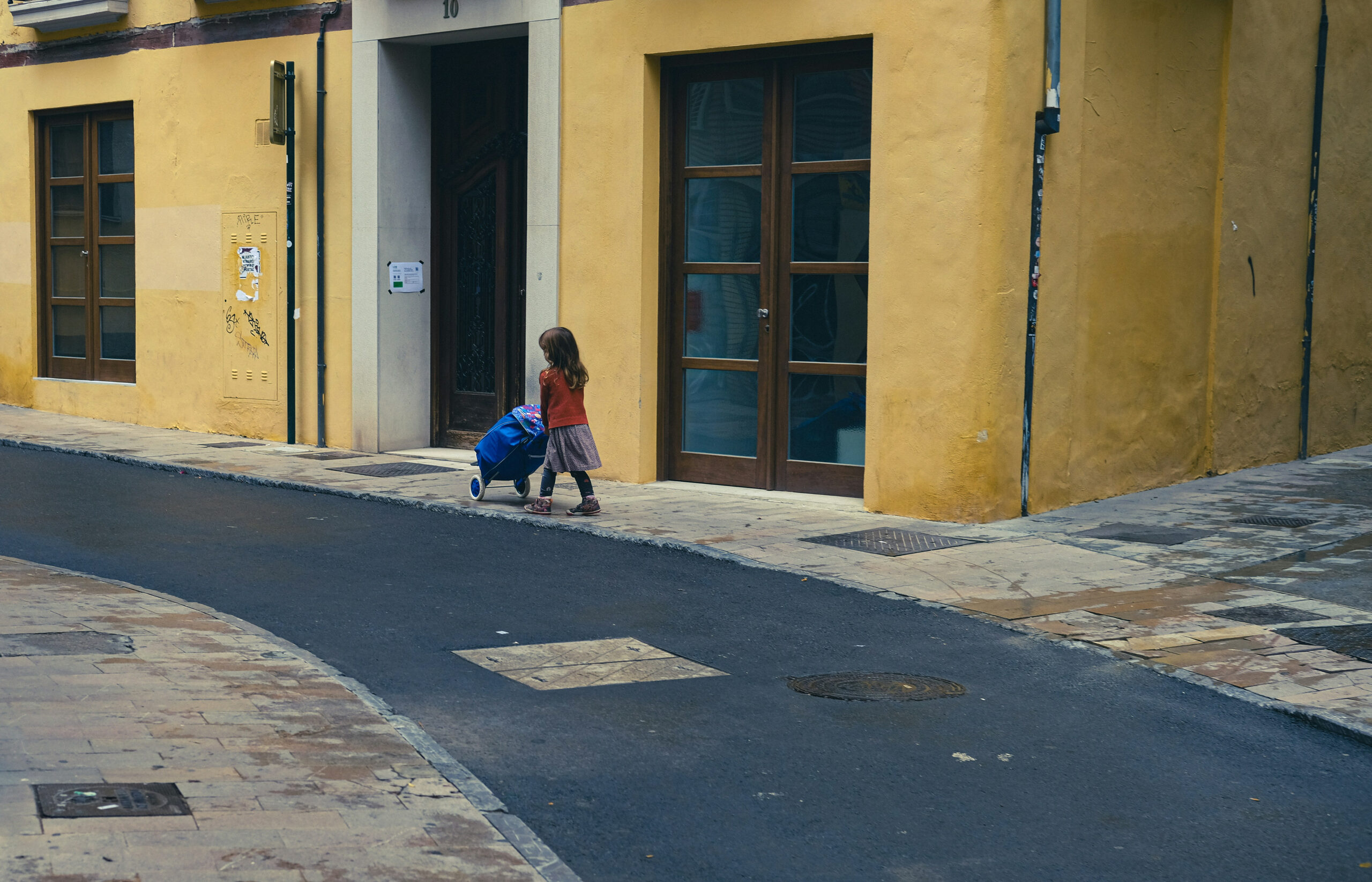 Young girl in red dress standing in a doorway on a cobblestone street